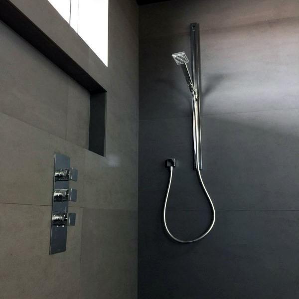 Minimalist shower with matte black walls, chrome handheld fixture, and recessed shelf.