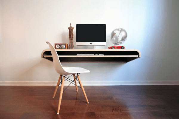 Minimalist desk setup with a computer, globe, model car, and chair on wooden floor