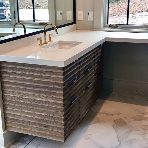 Bathroom vanity with wood-textured drawers, white countertop, and gold faucet.