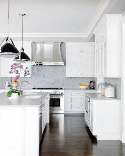 Bright white kitchen featuring herringbone backsplash, pendant lighting, and sleek stainless steel appliances.