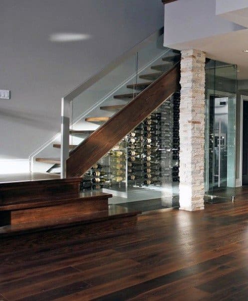 Modern staircase with glass railing beside a wine cellar, featuring a stone accent wall and rich, dark wine wood flooring