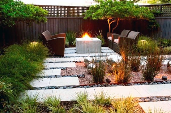 Modern patio with fire pit, minimalist chairs, ornamental grass, and decorative metal spheres.