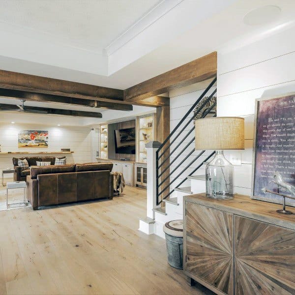 Farmhouse-style basement with wooden beams, shiplap walls, leather seating, and rustic decor.