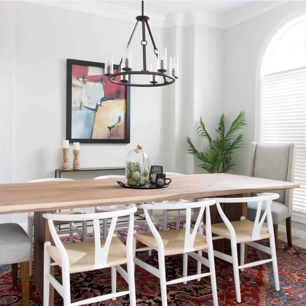 white dining room long wood table white chairs black metal chandelier framed wall art