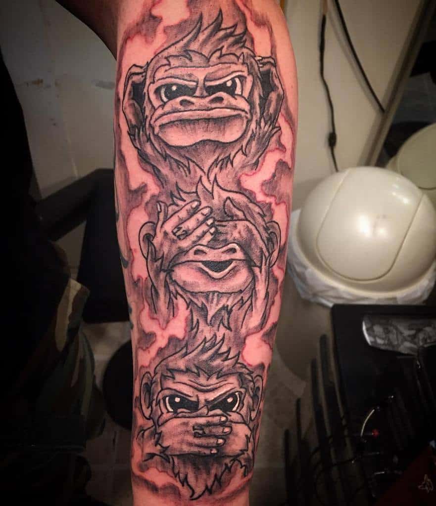 Forearm tattoo of three monkeys with "see no evil, hear no evil, speak no evil" poses, surrounded by fiery design