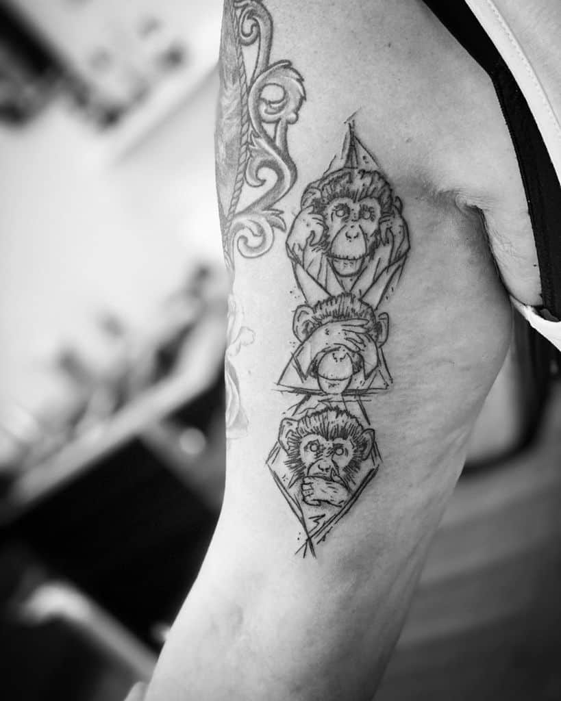 Black and white tattoo of three wise monkeys on a person's upper arm