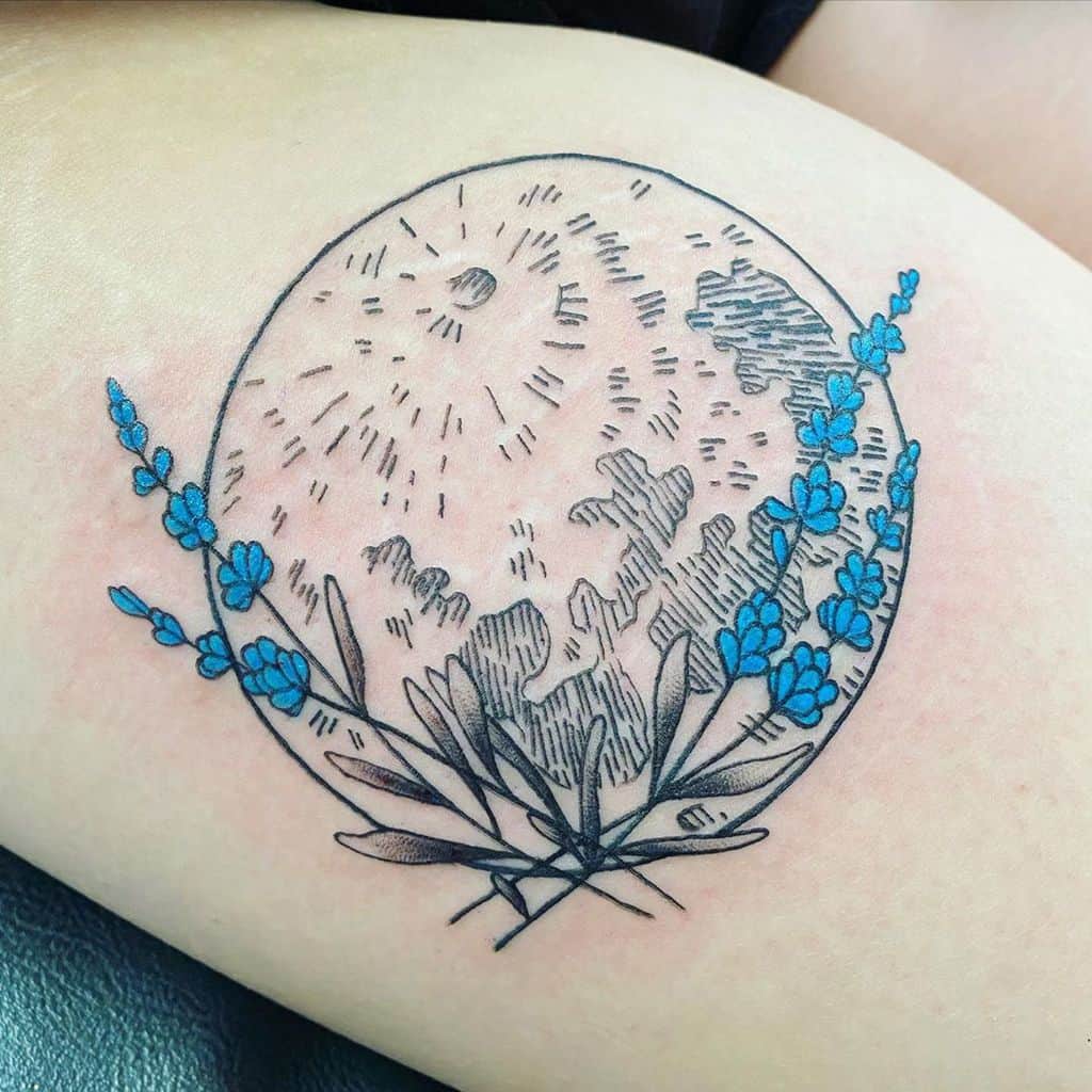 A tattoo of a circular design featuring the moon, surrounded by delicate blue flowers and leaves, placed on the upper arm.