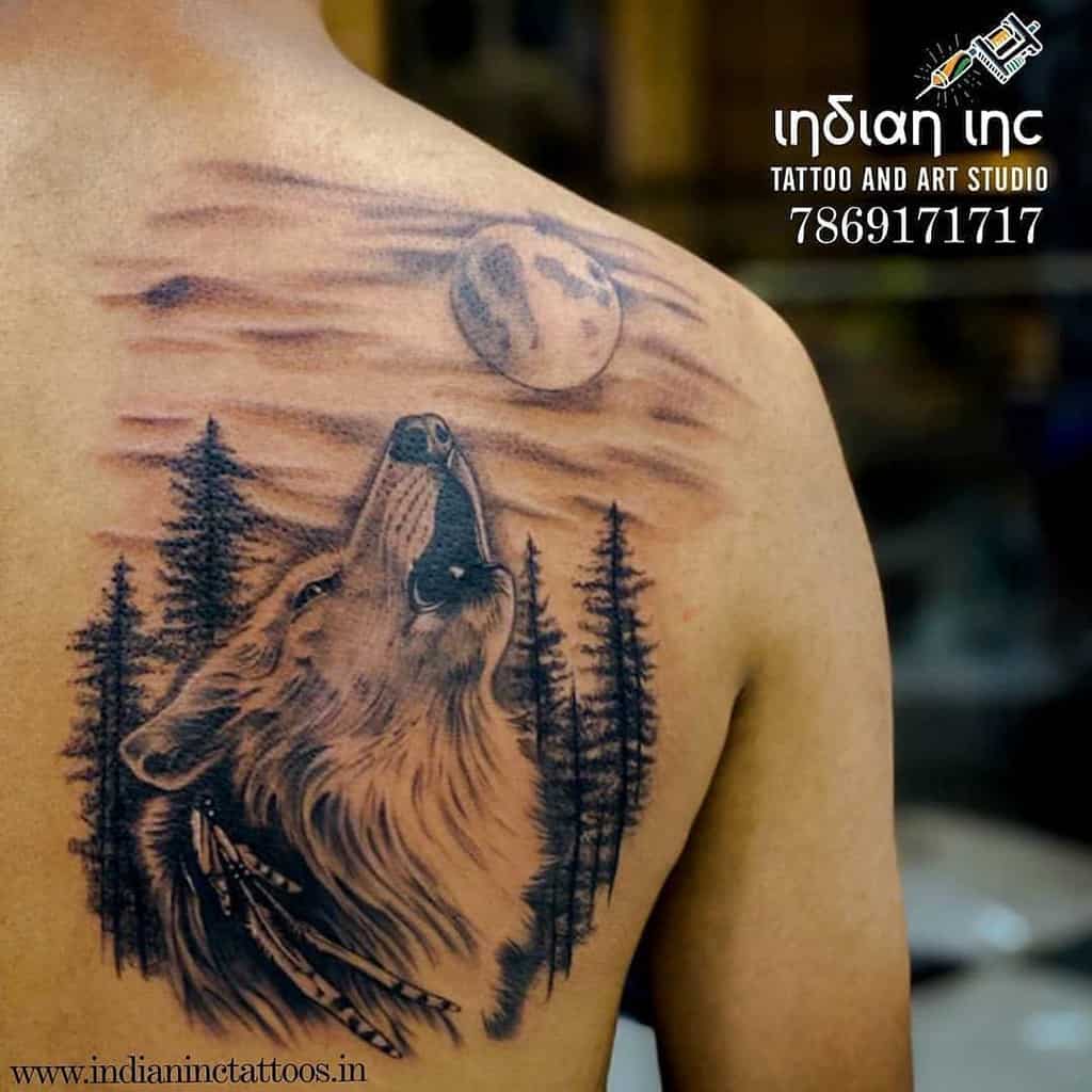 A striking tattoo of a lone wolf howling beneath a luminous moon, set against a dense forest backdrop, graces the person's shoulder