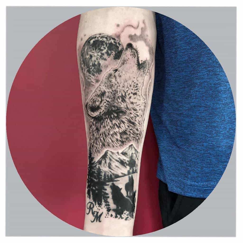 A captivating arm tattoo featuring a wolf howling at the moon, framed by serene mountains and towering trees, captures untamed wilderness with striking detail
