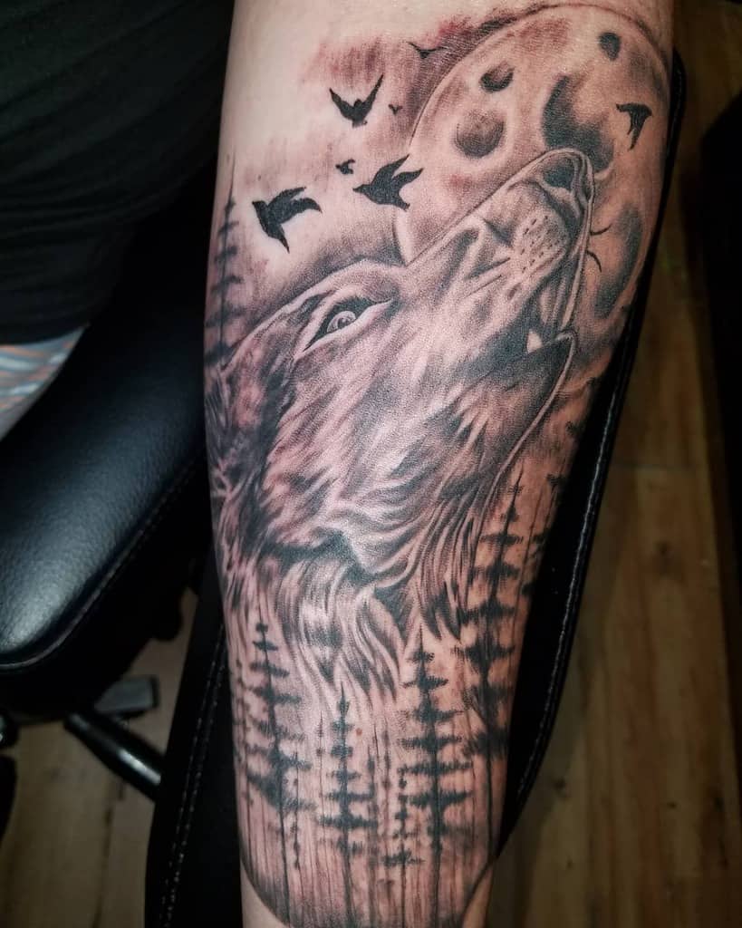A captivating tattoo of a lone wolf howling at the moon, surrounded by intricate trees and soaring birds in the background