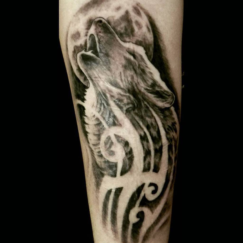 Tattoo of a howling wolf with tribal elements in black and grey ink