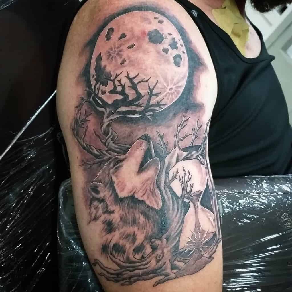 Tattoo of a wolf howling at the moon with trees on an upper arm