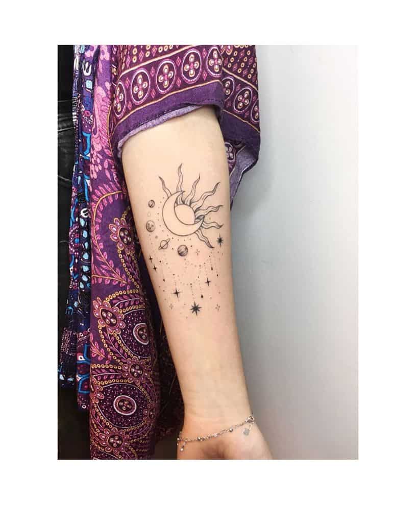 Minimalist tattoo of a sun and moon surrounded by stars and planets, featuring fine line details on the forearm.