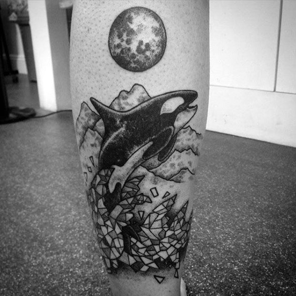 Black and gray tattoo on the lower leg, featuring an orca leaping through geometric shards with mountains and a moon above, creating a dynamic and surreal scene.