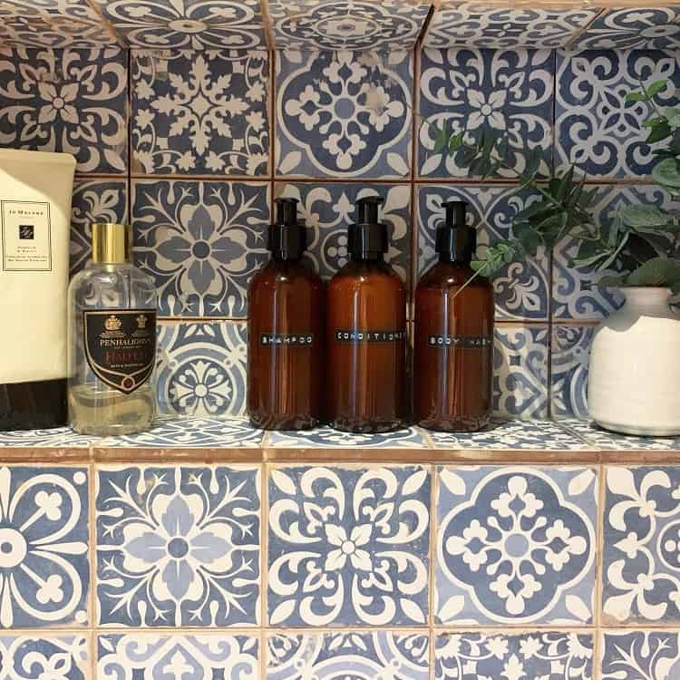 Moroccan-style bathroom recessed shelf with patterned tiles, amber bottles, and decor.