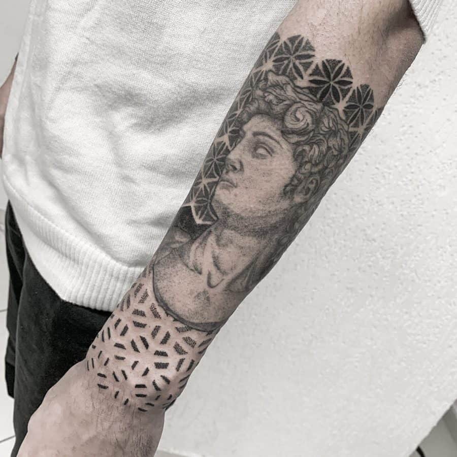 Forearm tattoo featuring a detailed Michelangelo’s David portrait blended with geometric patterns, creating a fusion of classical art and modern design.