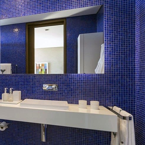 Modern bathroom with blue mosaic tiles, white floating sink, and large mirror.