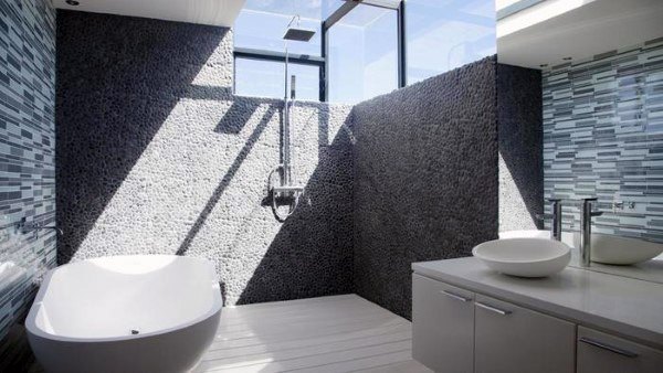 Modern bathroom with a shower, freestanding bathtub, stone accent wall, large mirrors, and natural light from skylights