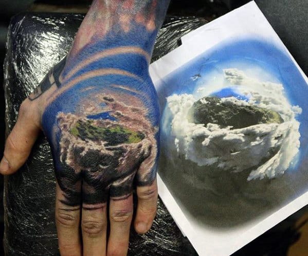 A hand tattoo of a clouded Earth-like orb next to a reference picture, with vibrant colors and detailed clouds