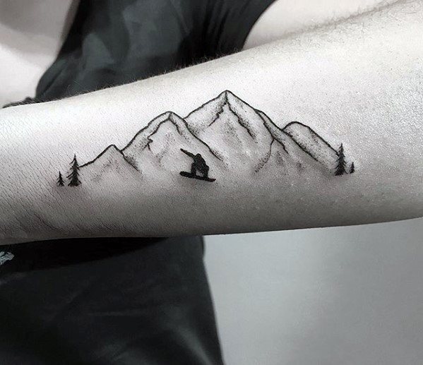 Minimalist tattoo of a snowboarder in action surrounded by mountain peaks and pine trees on the inner forearm.