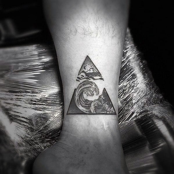Black ink geometric tattoo on the ankle featuring stacked triangles with a mountain, clouds, and a crashing wave, symbolizing nature's power and harmony.