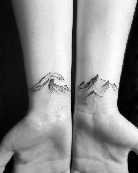 Minimalist wrist tattoos featuring a delicate wave on one side and a mountain range on the other, symbolizing balance between strength and fluidity.