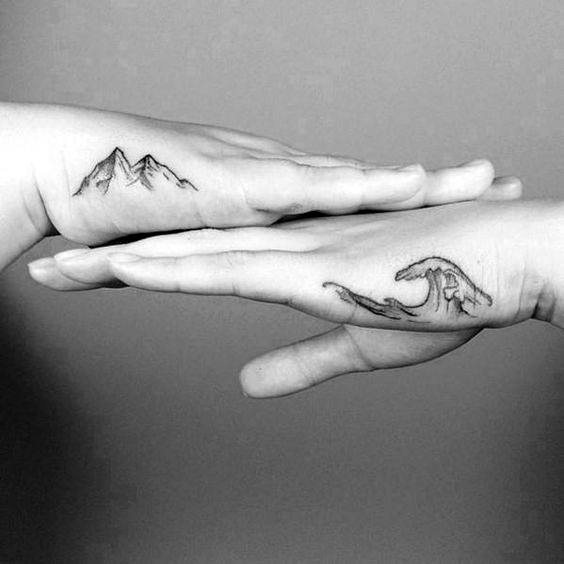 Two hands with tattoos: one of mountains and the other of ocean waves