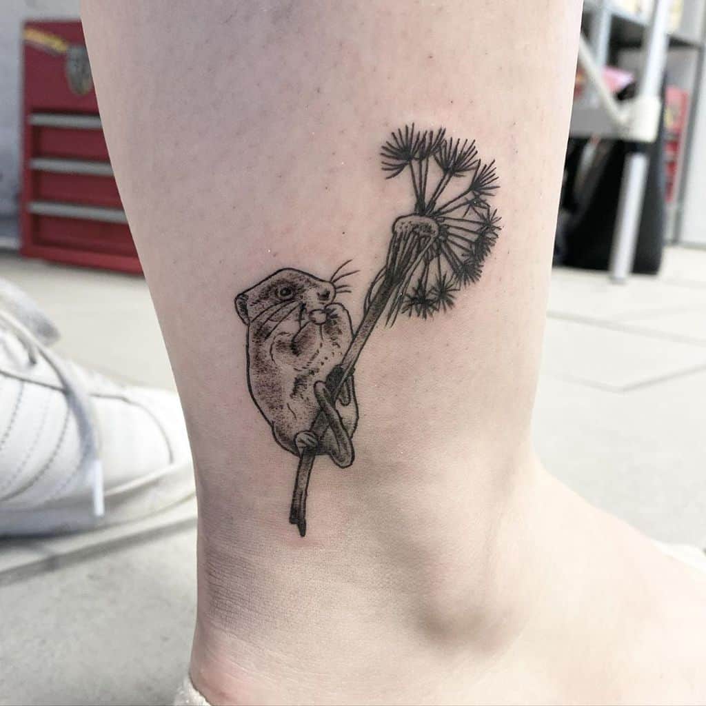 This tattoo creatively depicts a small animal holding a dandelion, blending playfulness and nature in a detailed and whimsical design.