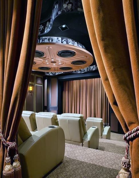 Luxurious home theater with plush beige recliners, an ornate ceiling, and elegant brown curtains framing the screen