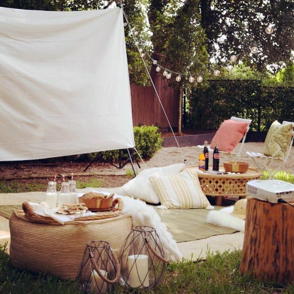 Cozy outdoor movie setup with soft cushions, a projector, and string lights for a relaxing evening.