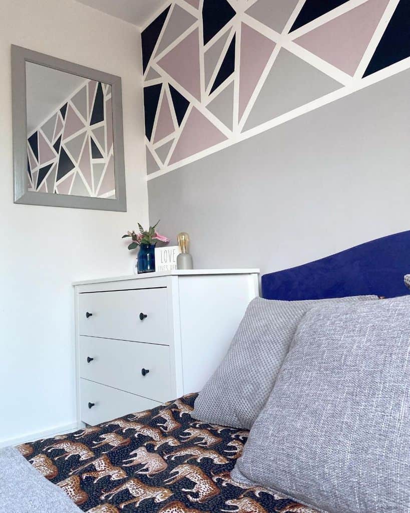Small bedroom with abstract geometric wall art, white dresser, and cozy bedding accents.