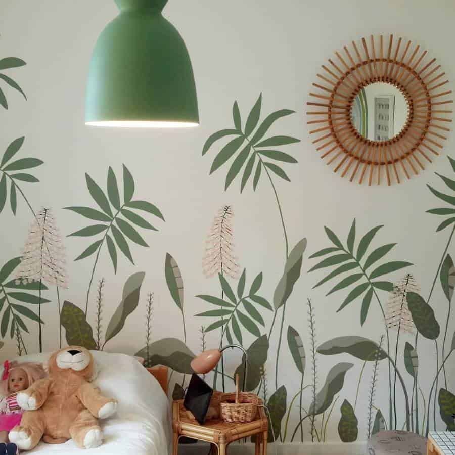 A cozy room with an accent wall, rattan mirror, green lamp, and a bed with a teddy bear and doll