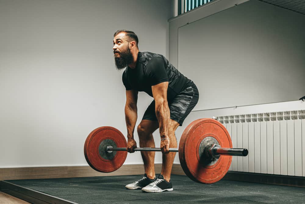 young muscular man in black sportswear lifting barbell in gym