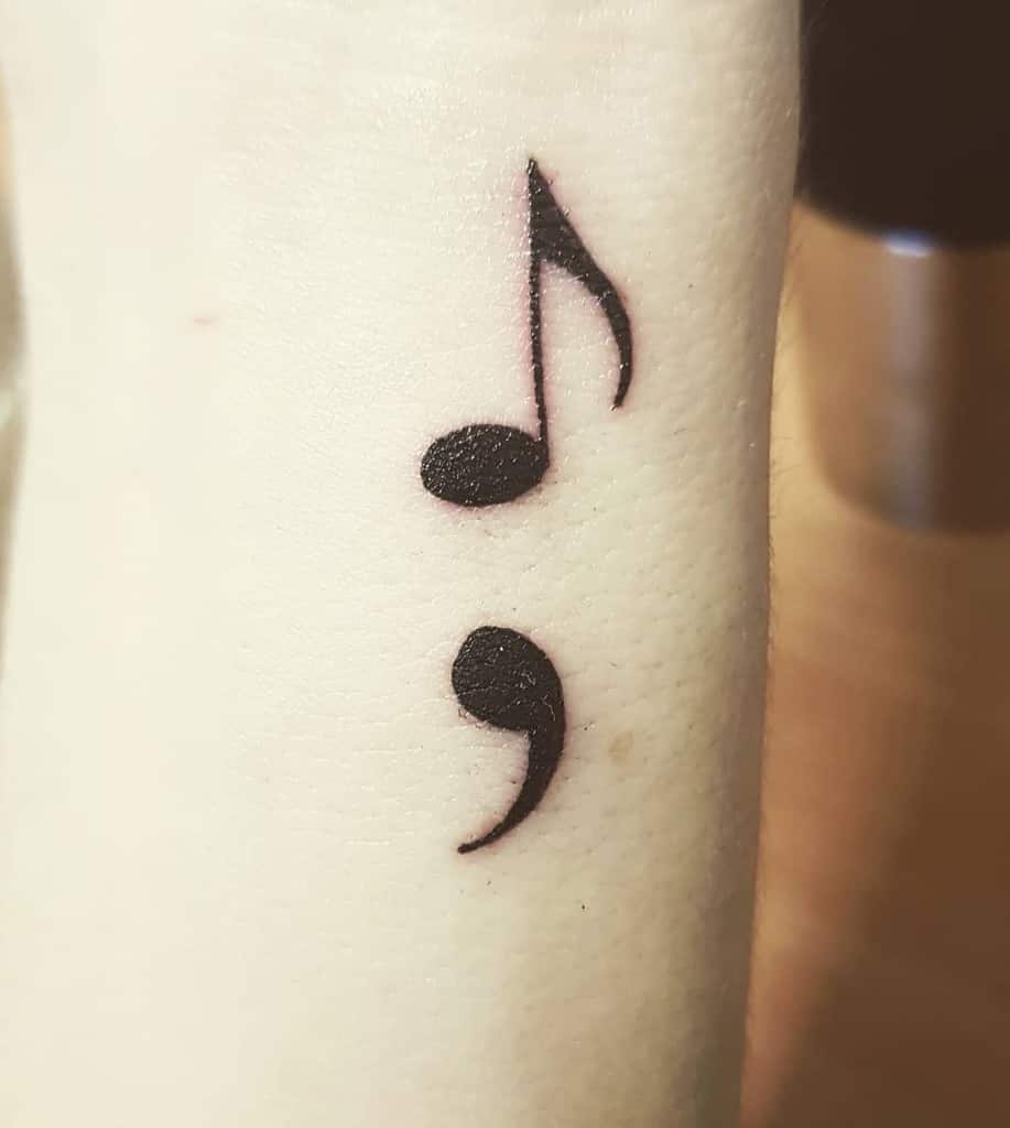 The tattoo features a combination of a musical note and a semicolon, placed artistically on the forearm.