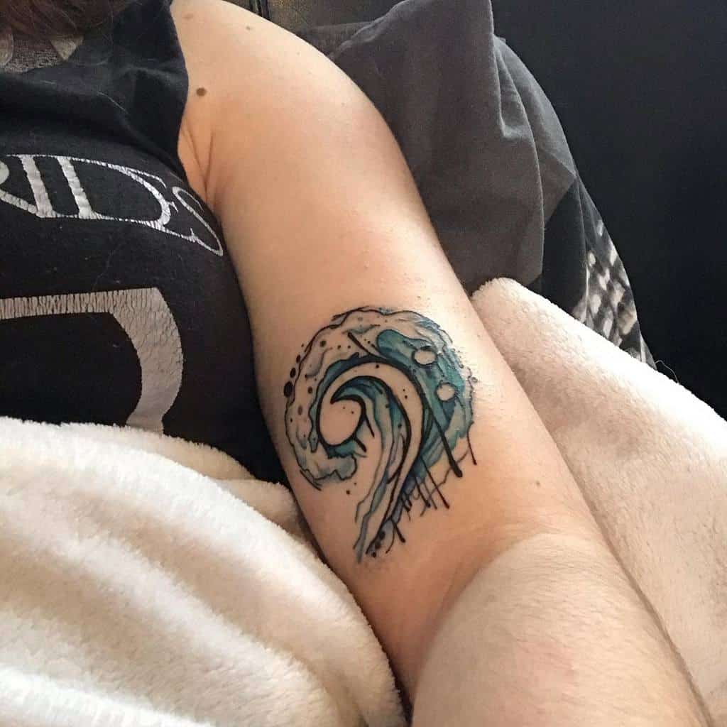 Watercolor-style tattoo of a curling ocean wave with blue and black ink splashes, featuring a bold, artistic design