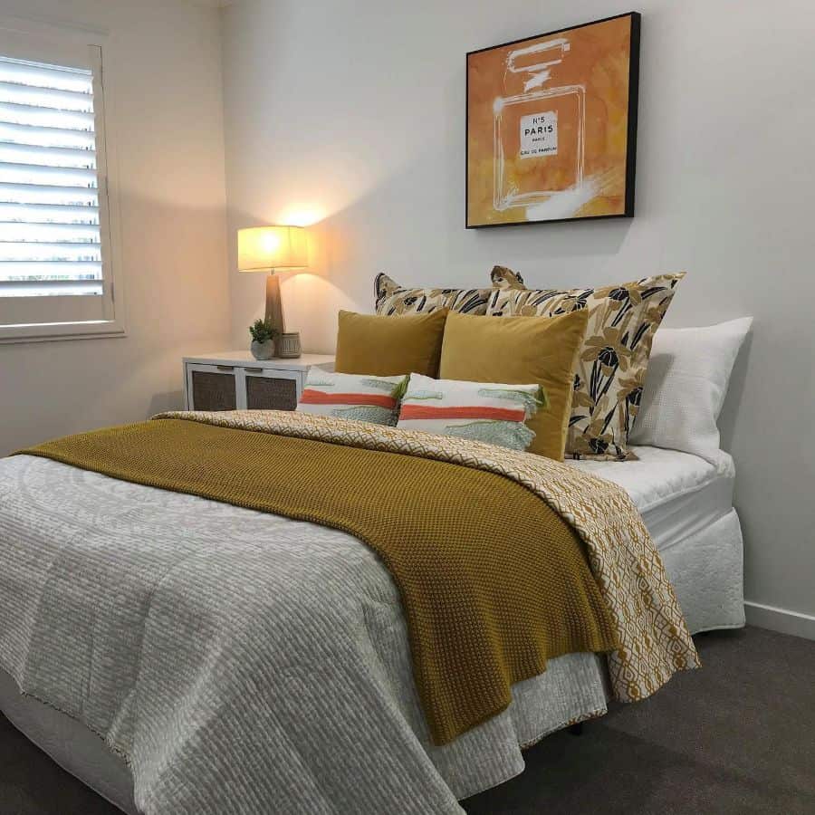 Cozy bedroom with a neatly made bed, yellow mustard blanket, decorative pillows, and artwork on the wall