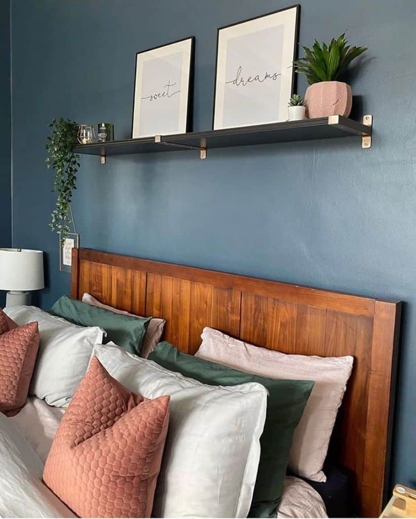 Modern muted blue bedroom with a wooden headboard, green and pink pillows, and a stylish shelf for decor.