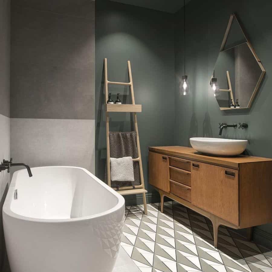 Modern bathroom with muted green walls, freestanding tub, wood vanity, and geometric tile floor.