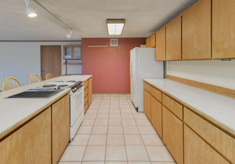 Simple and spacious kitchen with wooden cabinets, tiled flooring, and a warm red accent wall.