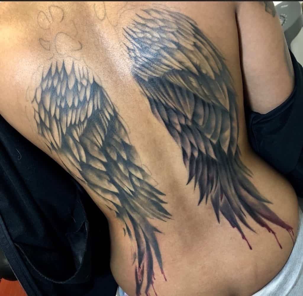 Dark angel wings tattoo featuring bold shading and a dripping blood effect
