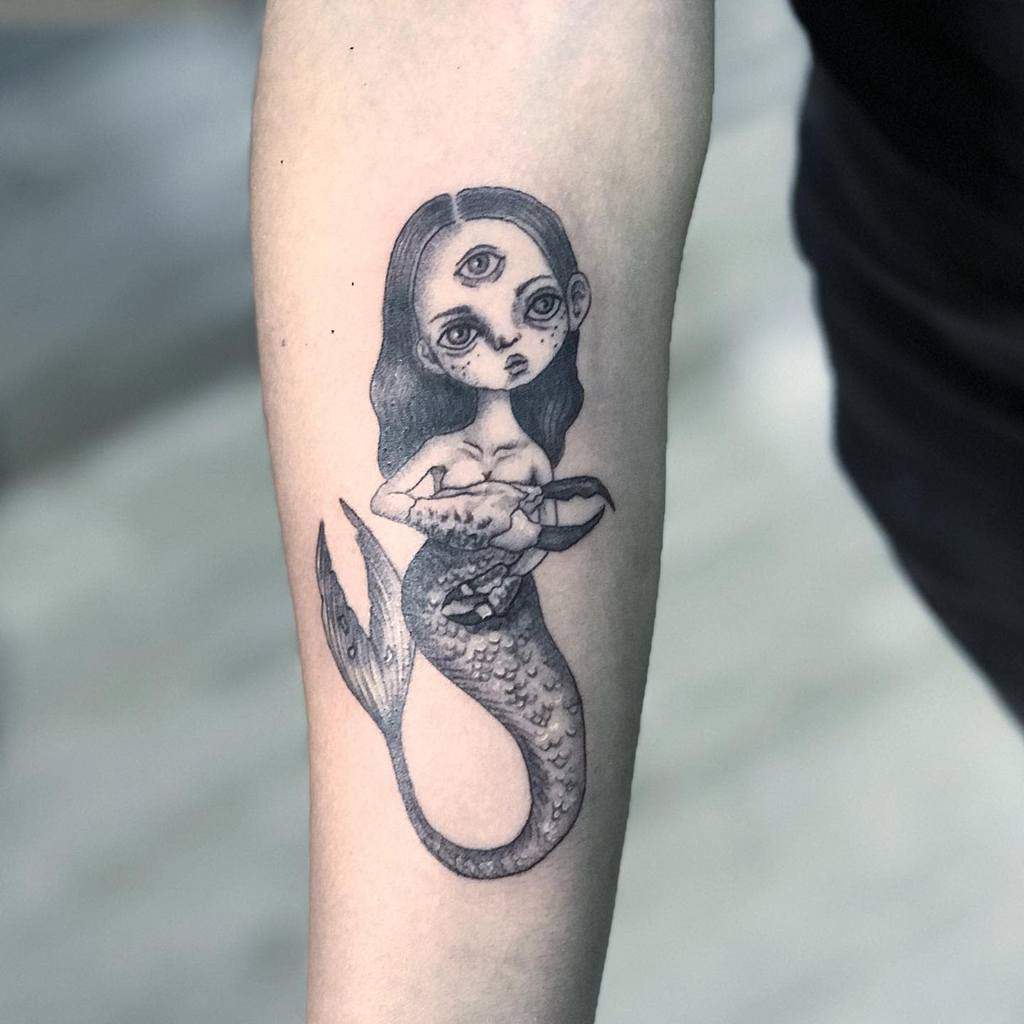 Tattoo of a three-eyed siren holding a seashell on a forearm