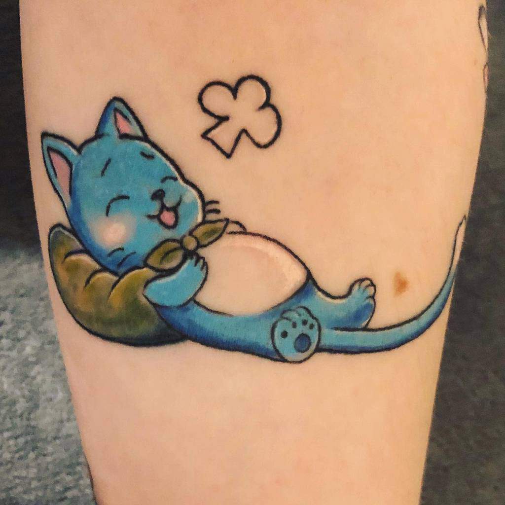 This tattoo features Happy from *Fairy Tail* peacefully sleeping on a pillow, with a content expression and a small clover thought bubble.