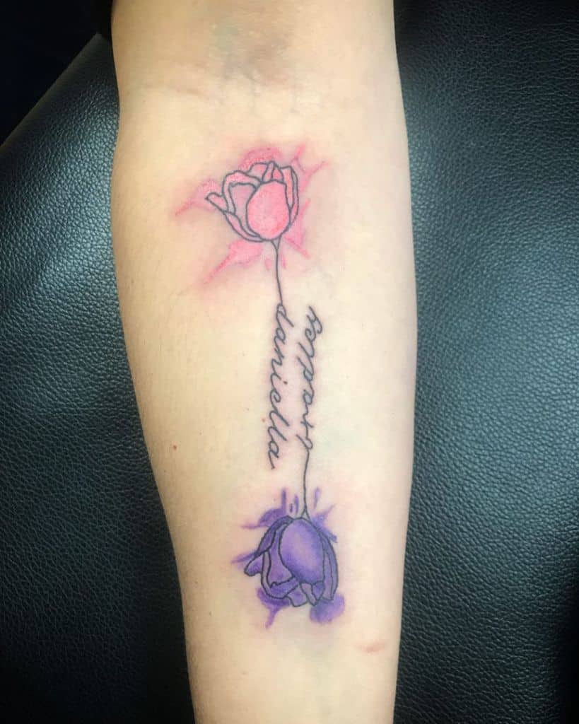 A forearm tattoo featuring two watercolor-style tulips, one pink and one purple, connected by a delicate cursive script reading "Rosas Daniella."