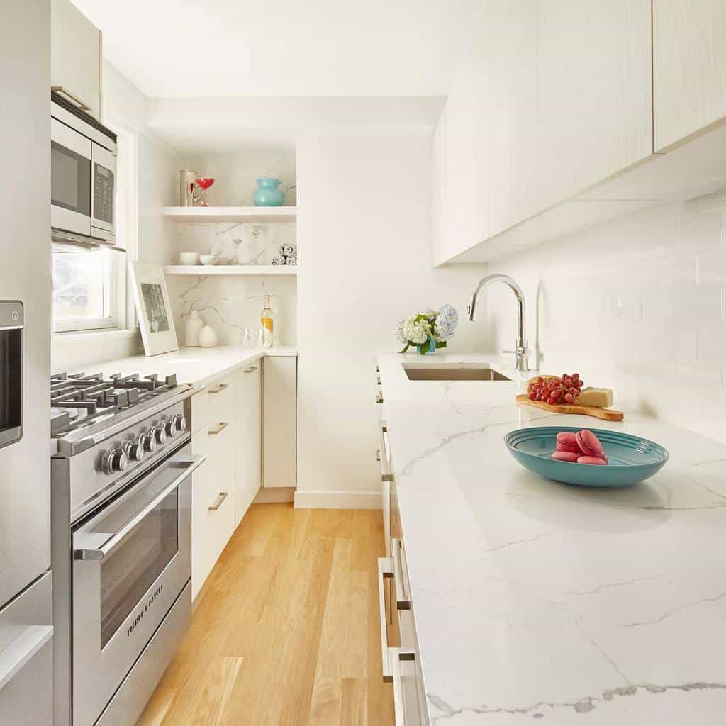 narrow galley kitchen white cabinets white marble countertop bowl of macarons