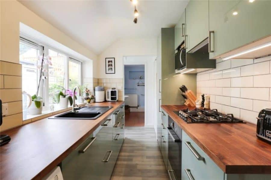 narrow galley kitchen green cabinets wood bench tops white tile splashback