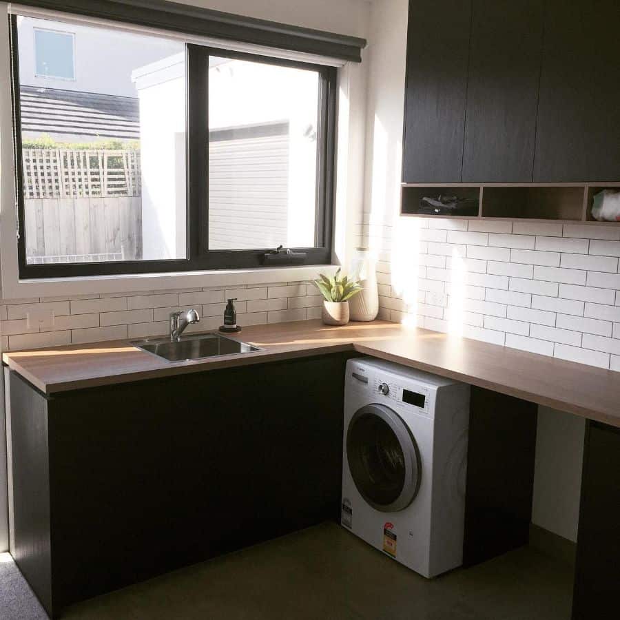 corner laundry with black cabinets and white tile wall