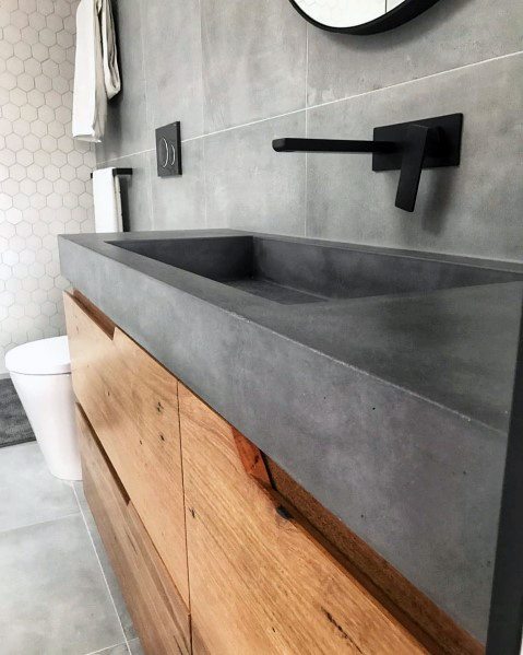 Natural wood vanity with concrete countertop and black wall-mounted faucet.