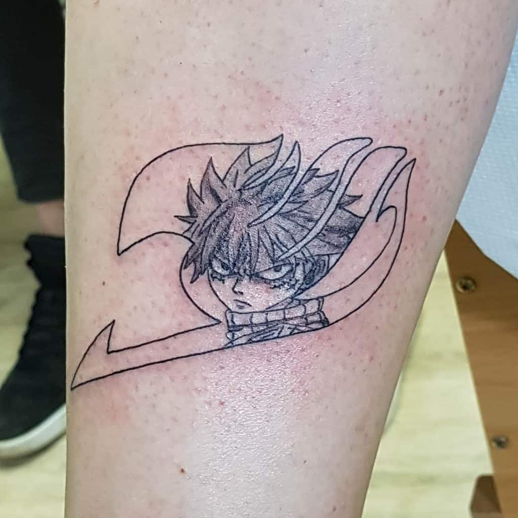 Minimalist black ink tattoo of Natsu Dragneel from Fairy Tail, featuring his intense expression inside the Fairy Tail guild emblem.