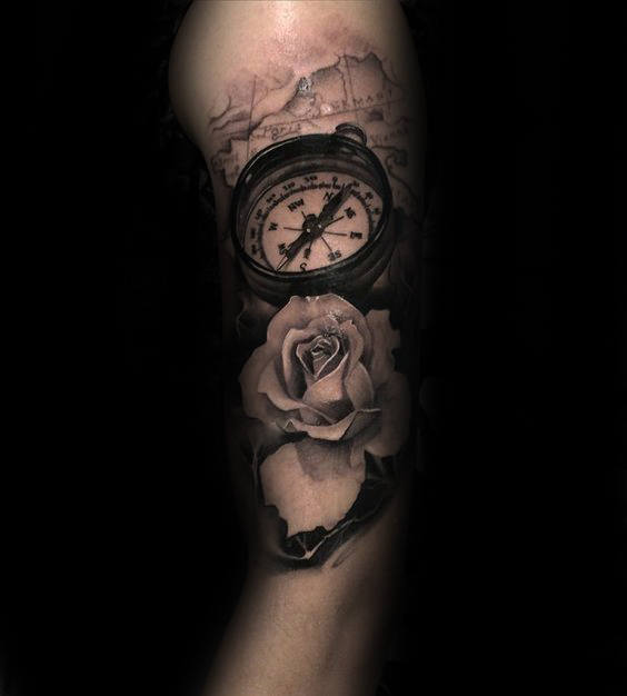 Tattoo of a compass and rose on upper arm in black and gray tones