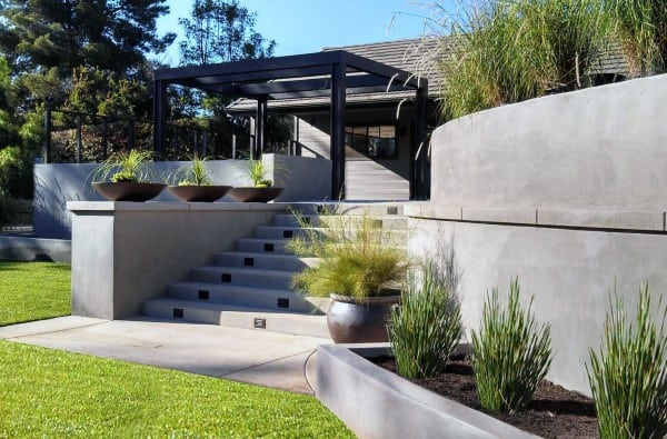 Concrete retaining walls with modern planters, stairs, and a pergola-covered patio area.